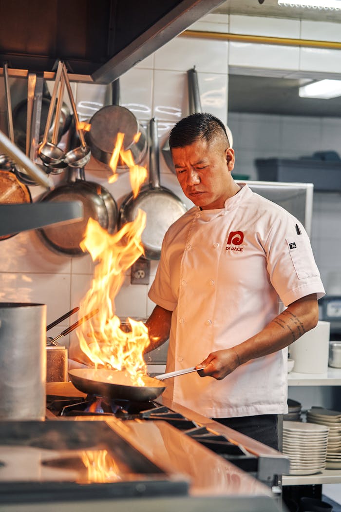 A chef expertly flambés in a restaurant kitchen, showcasing culinary skill and fire control.