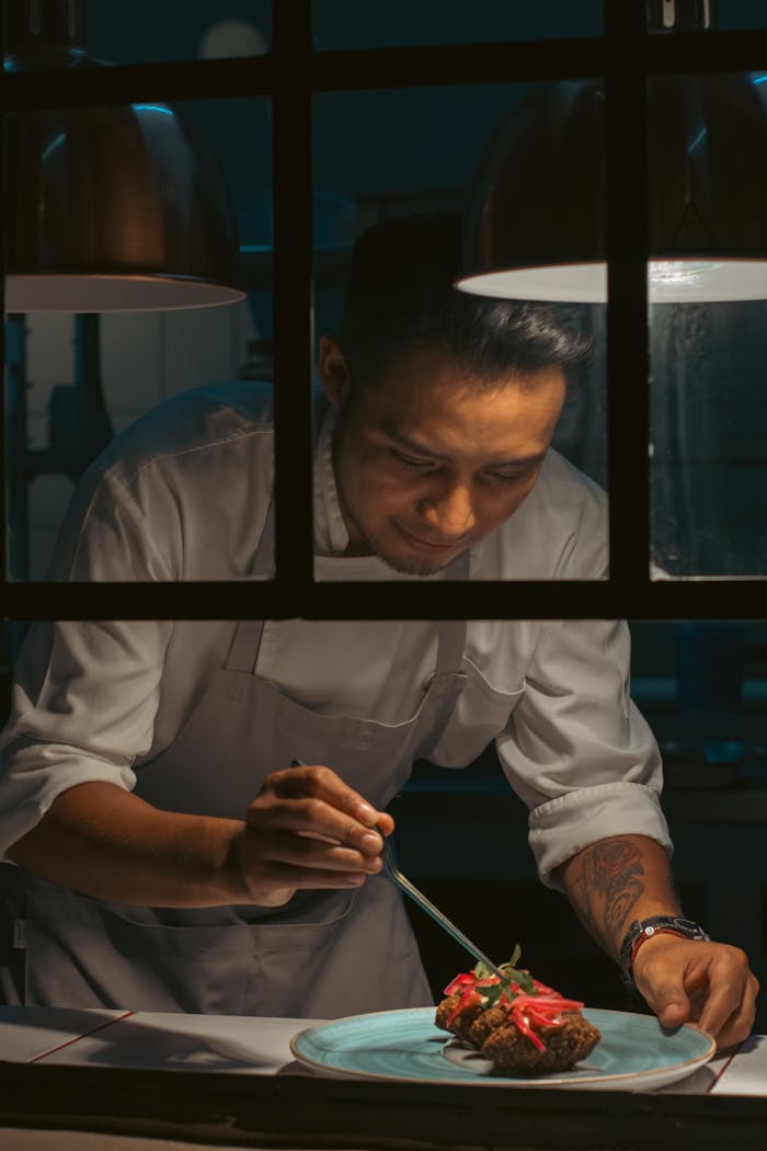 A focused chef meticulously plates a gourmet dish under warm lighting in a professional restaurant kitchen.